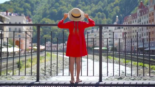 Liten flicka på hat på banvallen av en mountain river i en europeisk stad. — Stockvideo