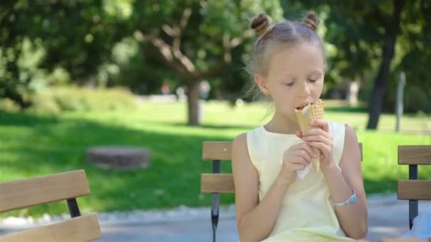 Маленькая девочка ест мороженое на открытом воздухе летом в кафе на открытом воздухе — стоковое видео