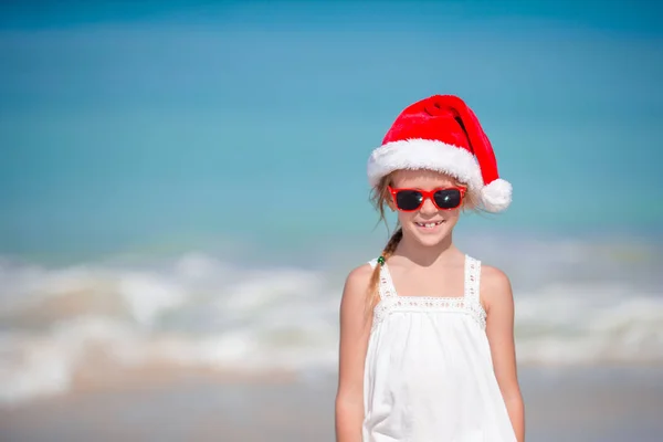 Adorable little girl in Santa hat on tropical beach — Stock Photo, Image