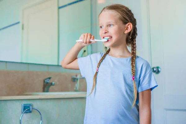Una chica adorable cepilla los dientes en el baño. Perfecta sonrisa blanca como la nieve de una niña — Foto de Stock