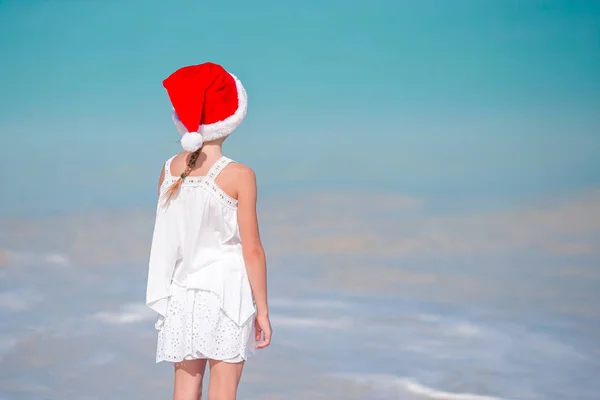 สาวน้อยที่น่ารักในหมวกซานต้าบนชายหาดเขตร้อน — ภาพถ่ายสต็อก