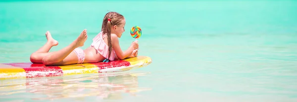 Lille jente med kjærlighet på pinne har det gøy på surfebrett i havet – stockfoto