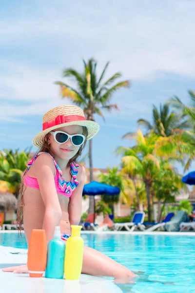 Menina com garrafa de creme solar sentado na borda da piscina — Fotografia de Stock