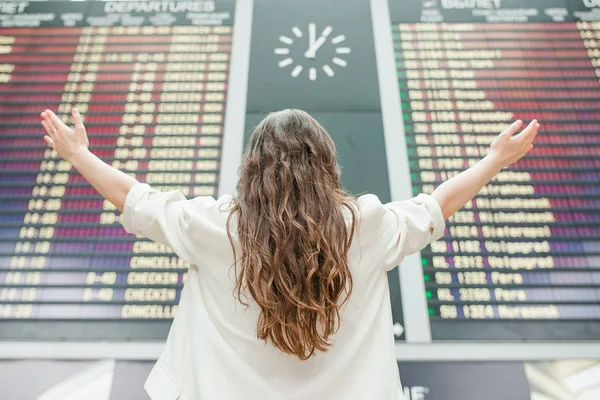 Молодая женщина в международном аэропорту глядя на борд информации о рейсе проверки на рейс — стоковое фото