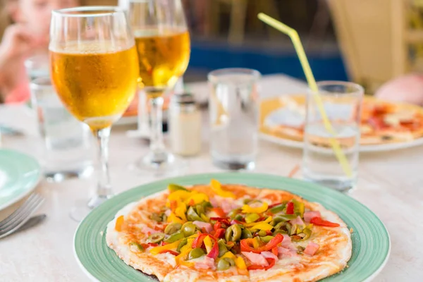 Pizza con queso mozzarella, oliva, tomate fresco y salsa de pesto. Se sirve en la mesa del restaurante con dos cervezas — Foto de Stock