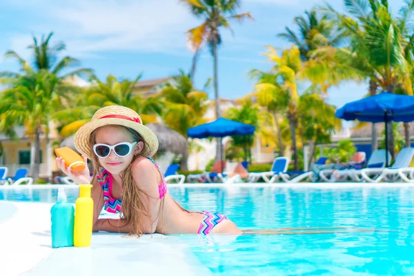 Niña con botella de crema solar en la piscina — Foto de Stock