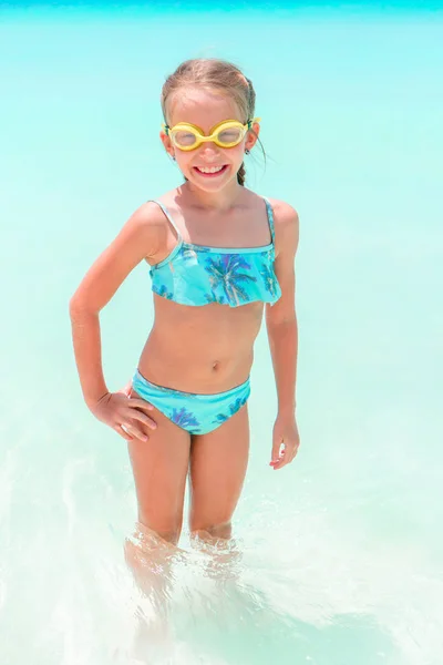 Petite fille heureuse éclaboussant et s'amusant dans l'eau peu profonde. Enfant en maillot de bain jouant avec le sable — Photo