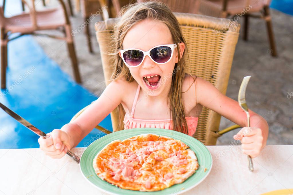 Portrait of cute little girl sitting by dinner table and eating pizza