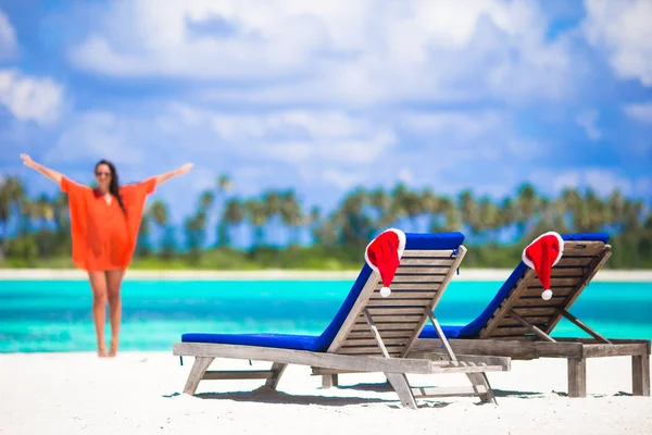 Concepto de Navidad: tumbonas de playa con sombreros rojos de Santa y hermosa chica durante las vacaciones tropicales —  Fotos de Stock