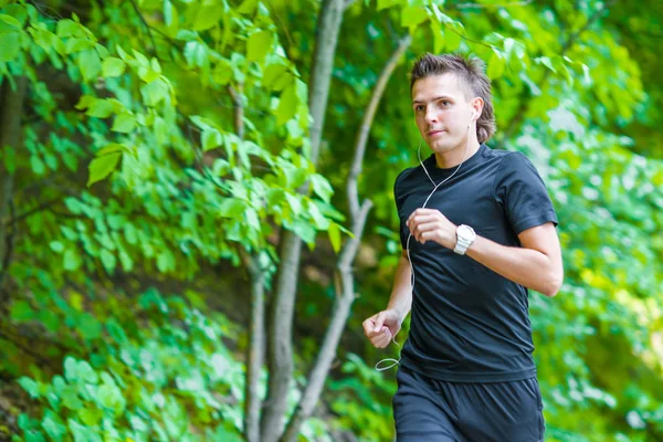 Sportowy sprawny młody człowiek joggingu podczas słuchania muzyki na świeżym powietrzu smarthphone — Zdjęcie stockowe