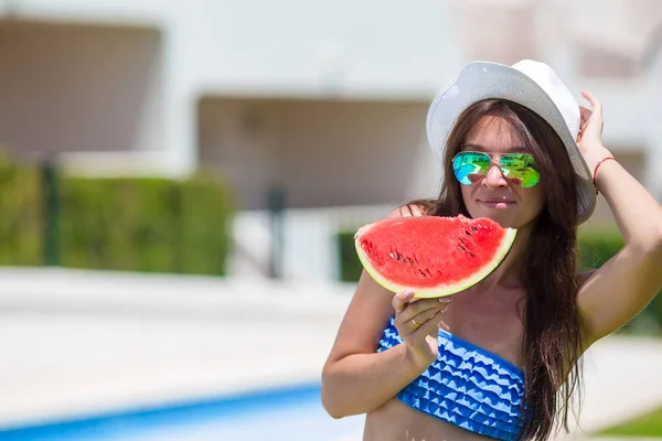 Jonge vrouw in hoed en zonnebril met watermeloen relaxen aan zwembad — Stockfoto