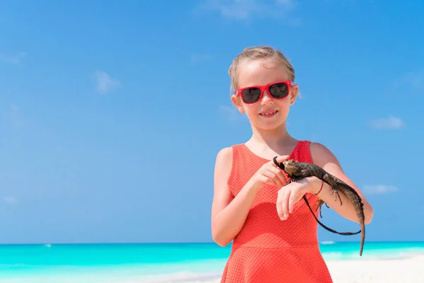 Adorable little girl happily holds a wild tropical lizard on white tropical beach — Stock Photo, Image