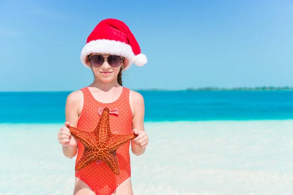 Bonne petite fille dans le chapeau de Père Noël pendant les vacances de plage de Noël ont beaucoup de plaisir — Photo