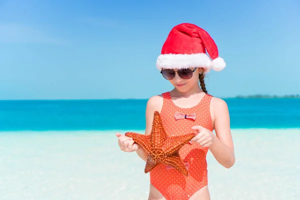 Glückliches kleines Mädchen mit Weihnachtsmütze im Weihnachtsurlaub am Strand haben eine Menge Spaß — Stockfoto
