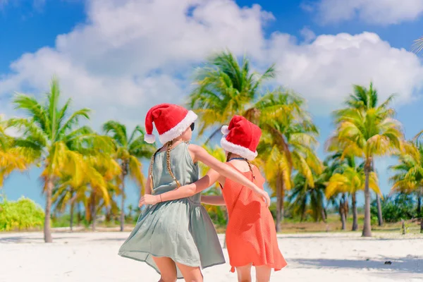 Las niñas adorables en los sombreros de Santa durante las vacaciones de playa se divierten juntas —  Fotos de Stock