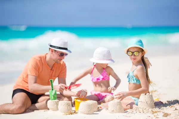 Vater und kleine Töchter basteln Sandburg am tropischen Strand — Stockfoto