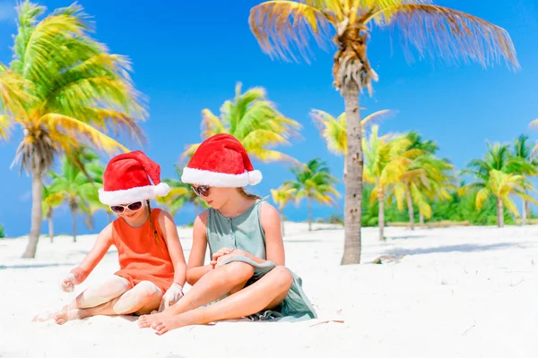 Kleine schattige meisjes in Santa hoeden tijdens strandvakantie hebben plezier samen — Stockfoto