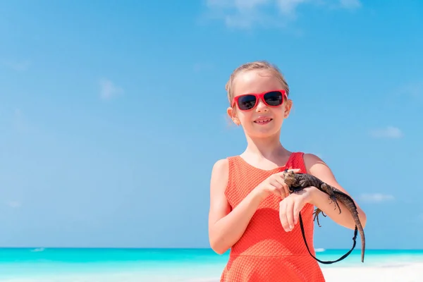 可爱的小女孩高兴地抱着一个野生热带蜥蜴在白色的热带海滩 — 图库照片