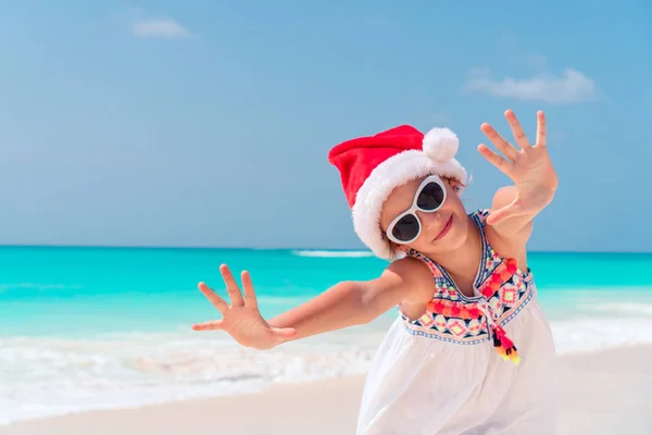 Entzückendes kleines Mädchen mit Weihnachtsmütze im Weihnachtsurlaub am Strand — Stockfoto