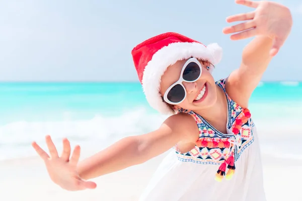 Entzückendes kleines Mädchen mit Weihnachtsmütze im Weihnachtsurlaub am Strand — Stockfoto