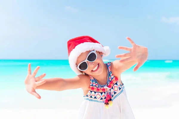 Urocza dziewczynka w kapeluszu Santa podczas świąt Bożego Narodzenia na plaży — Zdjęcie stockowe