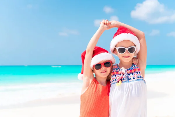 Kleine entzückende Mädchen in Weihnachtsmannhüten während des Strandurlaubs haben zusammen Spaß — Stockfoto