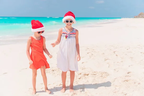 Piccole ragazze adorabili a Babbo Natale cappelli durante le vacanze al mare divertirsi insieme — Foto Stock
