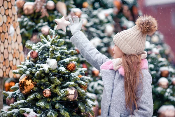 Kleines glückliches Mädchen in der Nähe von Tannenzweig im Schnee für Neujahr. — Stockfoto