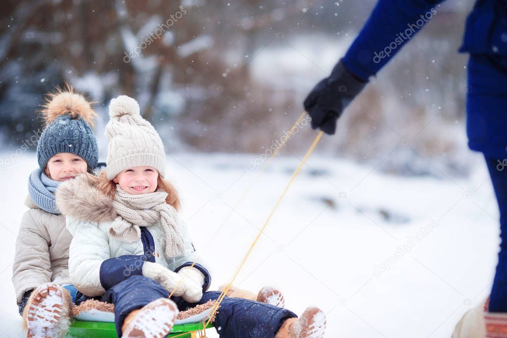 Little girls enjoy a sleigh ride. Child sledding. Children play outdoors in snow. Family vacation on Christmas eve outdoors
