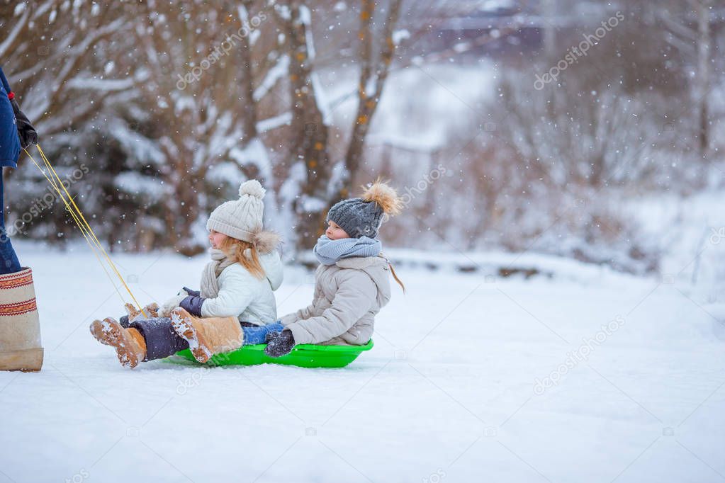 Adorable little happy girls sledding in winter snowy day.