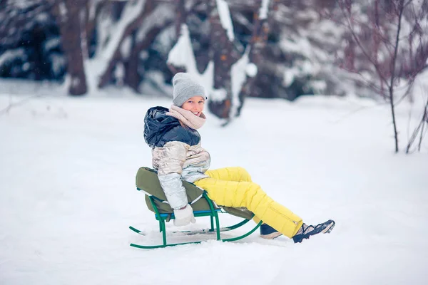 Schattig klein gelukkig meisje sleeën in de winter besneeuwde dag. — Stockfoto