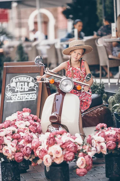 Bedårande liten flicka i hatt på mopeden utomhus — Stockfoto