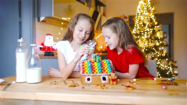 Små flickor gör jul pepparkakshus vid öppen spis i dekorerat vardagsrum. — Stockvideo