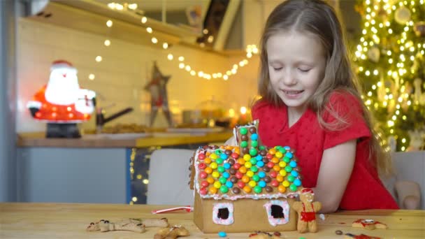Meisjes maken kerst peperkoek huis bij open haard in ingerichte woonkamer. — Stockvideo