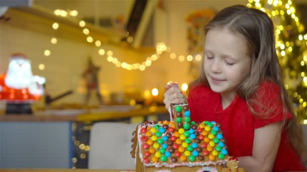 Meisjes maken kerst peperkoek huis bij open haard in ingerichte woonkamer. — Stockvideo