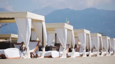 Akşam ışığında turkuaz bir denizin önünde tahta güneşlik yataklar. Forte dei Marmi 'deki ünlü İtalyan kumsalında güneşli yataklar.