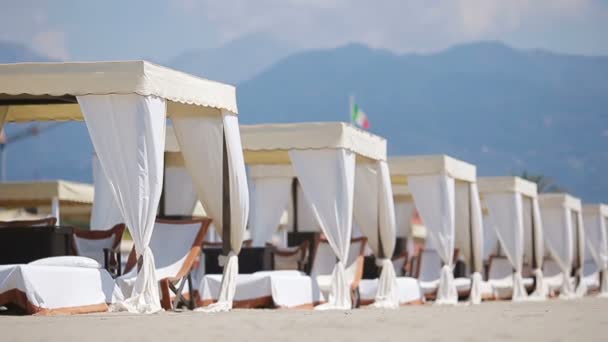 Tumbonas de madera frente a un mar turquesa a la luz de la tarde. Tumbonas en la famosa playa de arena italiana en Forte dei Marmi — Vídeo de stock
