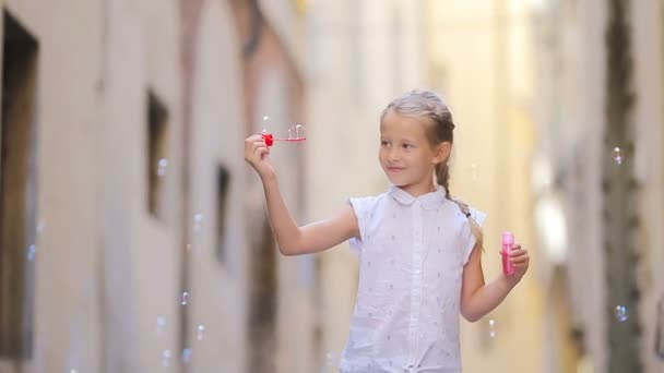유럽의 도시에서 야외에서 비누 거품을 불고 있는 사랑 스러운 어린 소녀. 로마에서 여름 방학을 보내고 있는 코카 시안 아이의 모습 — 비디오