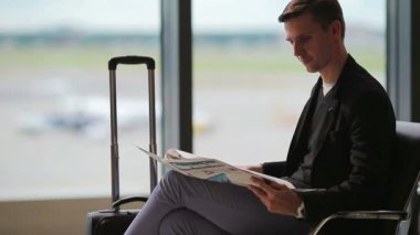 Gazete yatılı için beklerken havaalanında genç beyaz adamla. Elbise giyen sıradan genç işadamı.