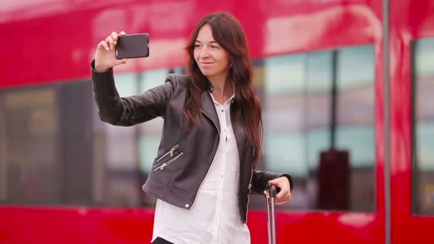 Ung kvinna med bagage tar selfie på en tågstation. Caucasiam turist väntar hennes expresståg medan hon reser. — Stockvideo