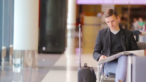 Młody człowiek kaukaski z gazety na lotnisku w oczekiwaniu na wejście na pokład. Dorywczo młody biznesmen sobie garnitur marynarka. — Wideo stockowe