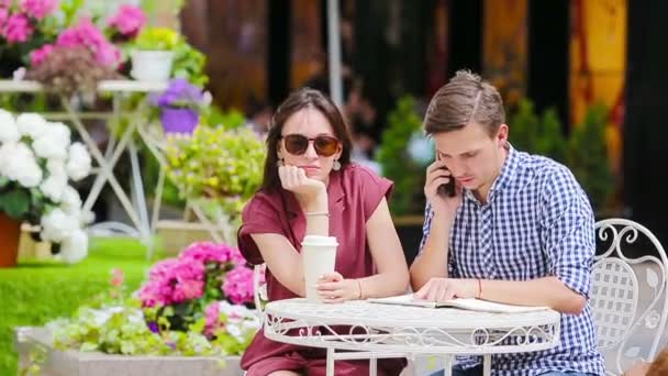 Jong koppel op outdoor cafe. Jong meisje is boos op haar vriendje omdat hij bezig met klusjes — Stockvideo