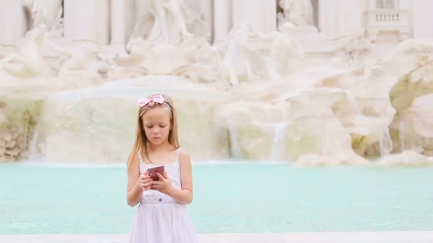 Adorable niña con teléfono inteligente en el cálido día al aire libre en la ciudad europea cerca de la famosa Fontana di Trevi — Vídeo de stock