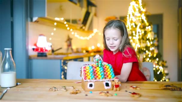 Små flickor gör jul pepparkakshus vid öppen spis i dekorerat vardagsrum. — Stockvideo