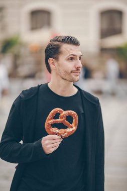 Beautiful young man holding pretzel and relaxing in park clipart