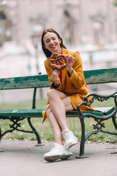 Schöne junge Frau hält Brezel in der Hand und entspannt sich im Park — Stockfoto