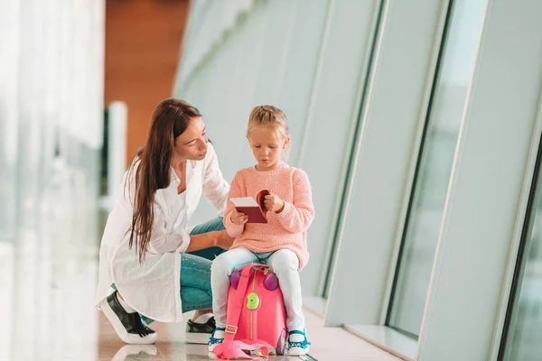 Familia feliz en el aeropuerto sentada en la maleta con tarjeta de embarque esperando el embarque —  Fotos de Stock