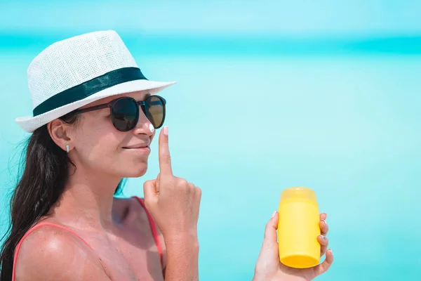 Mujer joven aplicar crema en la nariz en la playa — Foto de Stock