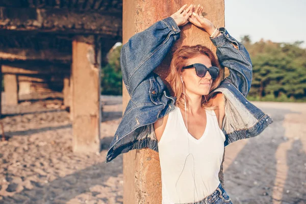 Utomhus mode porträtt av snygg tjej klädd i jeans jacka på stranden. — Stockfoto