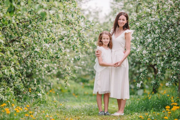 Adorável menina com jovem mãe em flor cereja jardim no belo dia de primavera — Fotografia de Stock